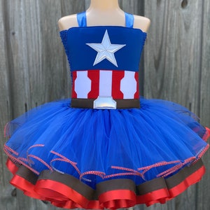 May include: A blue tulle tutu with red and brown ribbon trim. The top of the tutu is a blue and red fabric with a white star and a brown belt.