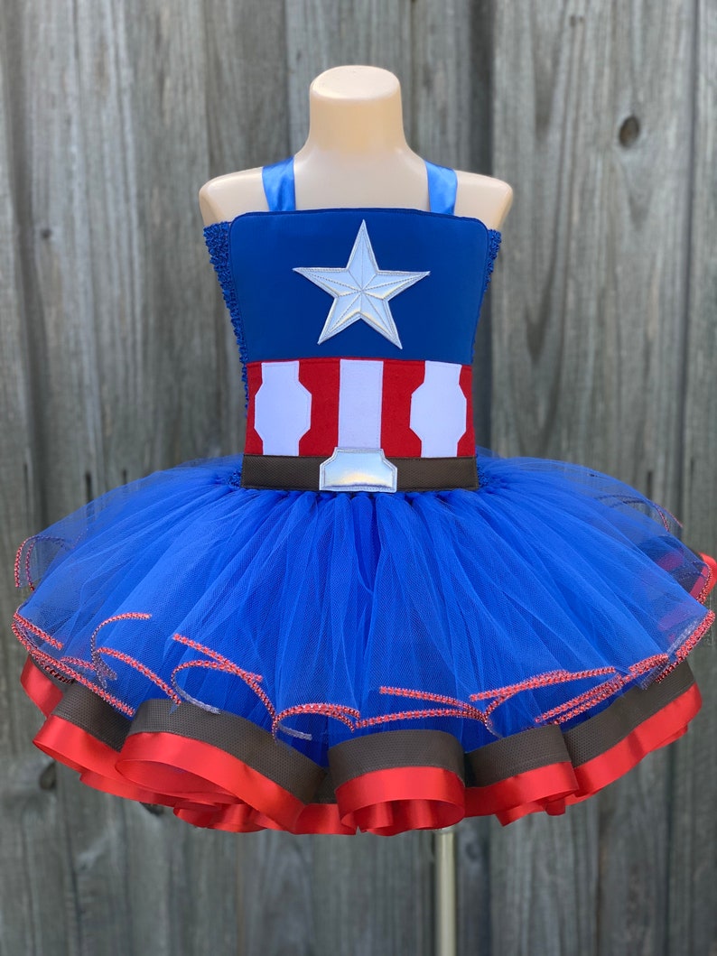 May include: A blue tulle tutu with red and brown ribbon trim. The top of the tutu is a blue and red fabric with a white star and a brown belt.