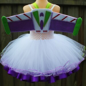 May include: White tulle tutu with purple satin ribbon trim and a purple felt Buzz Lightyear costume wing with green and white accents.