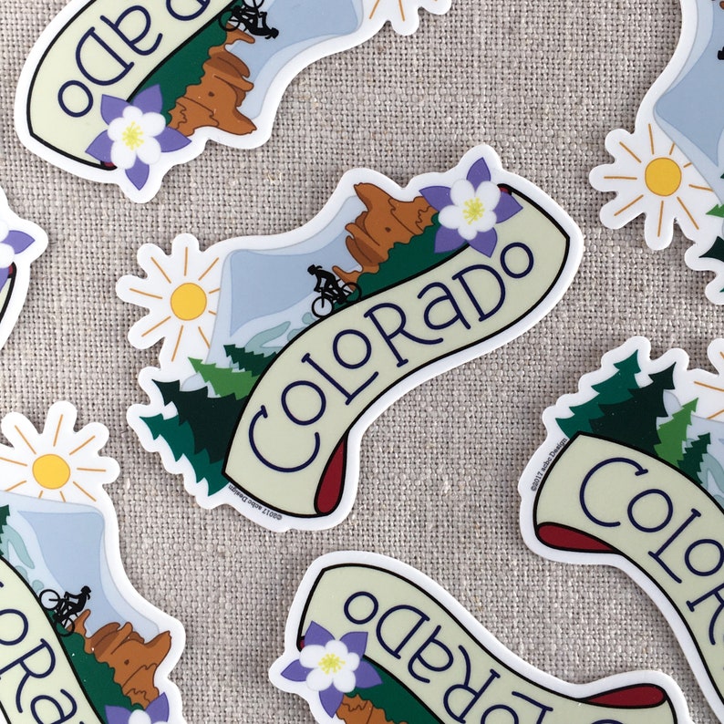 Several illustrated Colorado vinyl stickers scattered on a neutral background.