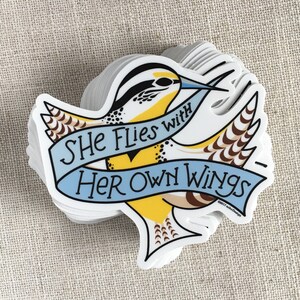 A stack of She Flies with Her Own Wings vinyl stickers on a neutral background.