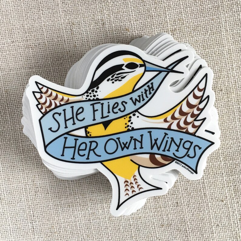 A stack of She Flies with Her Own Wings vinyl stickers on a neutral background.