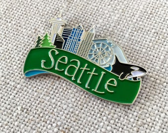 Può includere: Spilla in smalto verde e argento con uno skyline di Seattle, Washington. La spilla include la Space Needle, una ruota panoramica e un'orca. Il testo "Seattle" è scritto su uno stendardo verde.