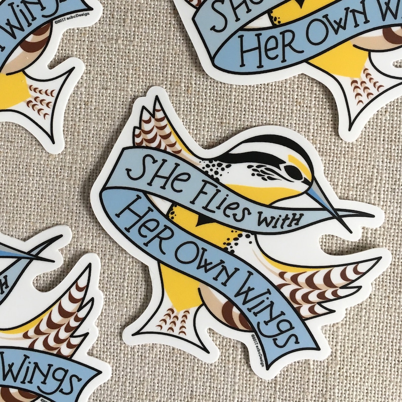 Several She Flies with Her Own Wings vinyl stickers, scattered on a neutral background.