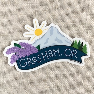 May include: A sticker with a blue banner that says "GRESHAM, OR" with a mountain, a sun, and purple flowers. The sticker has a copyright notice that says "©2019 abc Design".