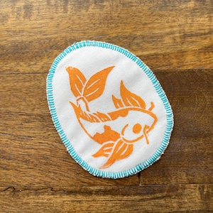 May include: A white fabric patch with a blue stitched border featuring an orange koi fish design.