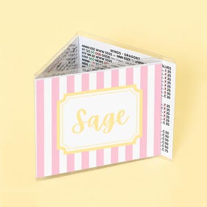 Puede incluir: Una cartera de pl&aacute;stico transparente con rayas verticales rosas y blancas. La cartera tiene una etiqueta amarilla y blanca con el nombre "Sage" en cursiva. La cartera est&aacute; abierta, revelando texto en el interior.