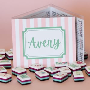 Puede incluir: Un tarjetero a rayas rosas y blancas con el nombre "Avery" en escritura verde. Peque&ntilde;as baldosas cuadradas decorativas con dise&ntilde;os florales y geom&eacute;tricos est&aacute;n dispersas frente al tarjetero.