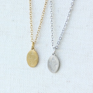 May include: Two necklaces with oval pendants, one gold-toned and one silver-toned. Each pendant features a detailed figure. The chains are delicate and the pendants are small, creating a minimalist jewelry design.