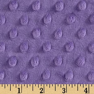 May include: Close-up of a lavender minky fabric with a textured, dotted pattern. The fabric has a soft, plush appearance. A wooden ruler with inch markings is at the bottom of the image.