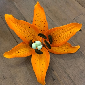 May include: A single orange lily with black spots and a light green centre. The lily is lying flat on a wooden surface.