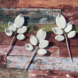 May include: Three white sugar paste leaf sprigs with five leaves each, on a rustic wooden background.