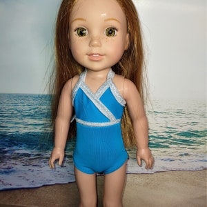 May include: A doll wearing a blue swimsuit with silver trim. The swimsuit has a halter top and a criss-cross design in the front. The doll has long, straight, light brown hair and green eyes.