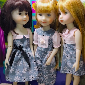May include: Three dolls wearing floral print dresses. The dolls have long hair and are wearing different colored dresses. The dolls are standing in front of a colorful background.