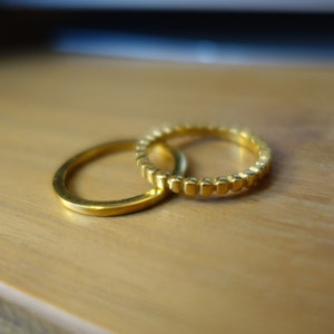 Peut inclure: Deux bagues en or, l'une avec une surface lisse et l'autre avec une surface texturée, sont empilées l'une sur l'autre.