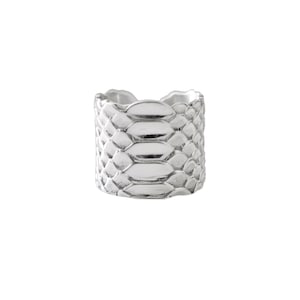 Peut inclure: Une bague en argent avec un motif texturé en forme d'écailles. La bague est large et a un bord supérieur légèrement irrégulier. Le design ressemble à de la peau de serpent ou de reptile. La bague est sur fond blanc.