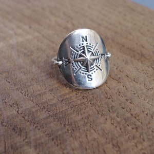 Peut inclure: Une bague en argent avec un motif de boussole. La boussole présente une étoile au centre avec les lettres N, S, E et W autour.