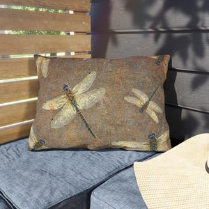 May include: A brown throw pillow with a dragonfly pattern. The pillow has a distressed, vintage look and features multiple dragonflies in various shades of brown, yellow, and blue.
