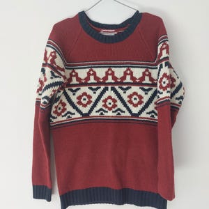 May include: A red, white, and blue patterned sweater with a crew neck and long sleeves.