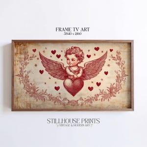 Puede incluir: Una impresión enmarcada con una ilustración vintage de un querubín sosteniendo un corazón, rodeado de corazones y estrellas. La obra de arte está en tonos rojos y marrones, con el texto "FRAME TV ART" y "STILLHOUSE PRINTS" visible.