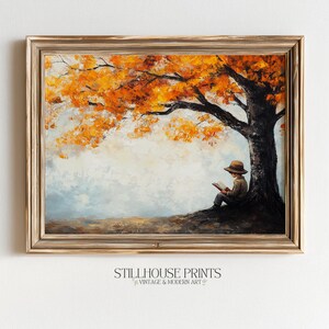 May include: A framed oil painting depicting a person wearing a hat sitting at the base of a large tree with vibrant orange autumn leaves. The person is reading an open book. The scene features a light-colored sky and a dark, textured tree trunk.
