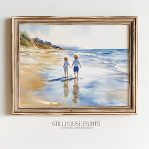 Puede incluir: Impresión en acuarela enmarcada de dos niños en una playa, mirando al mar. La obra de arte presenta un marco dorado y una escena costera serena con tonos azules y beige. La impresión incluye el texto "STILLHOUSE PRINTS VINTAGE & MODERN ART".