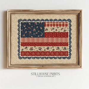 May include: Framed artwork featuring a quilted American flag design. The flag incorporates red and white stripes, a blue field with floral patterns, and a scalloped blue border. The frame is gold-toned, and the artwork is labeled "Stillhouse Prints."