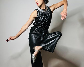 May include: A black jumpsuit featuring a sleeveless top with a decorative neckline and wide-leg trousers. The outfit is completed with silver metallic shoes. The jumpsuit is made of a shiny material, creating a modern and stylish appearance.