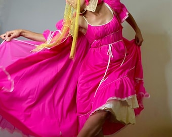 May include: A vibrant fuchsia dress with a flowing skirt and white trim. The dress features a square neckline and a layered skirt. A matching cape and headpiece with pink accents and yellow netting complete the ensemble. The outfit is a bold statement.