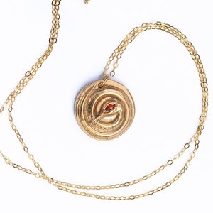 May include: A gold necklace with a round pendant featuring a coiled snake design with a red gemstone eye.