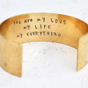 May include: Gold metal cuff bracelet with the inscription "You are my love my life my everything".