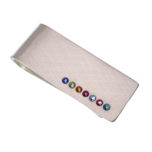 May include: A silver money clip with a row of colorful gemstones. The gemstones are set in a line along the clip and are in the colors of the rainbow.