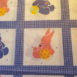 May include: White fabric with a blue grid pattern.  The fabric features a repeating pattern of pink and blue bears and bunnies holding balls.  The bears and bunnies have hearts on their chests.