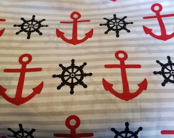 May include: White fabric with a repeating pattern of red anchors and black ship wheels. The anchors have a simple design with a crossbar and a rounded top. The ship wheels have eight spokes and a central hub.