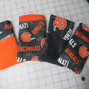 May include: Four fabric items with a Cincinnati Bengals theme. The items are primarily black and orange, featuring the team's logo and the words "Bengals" and "Cincinnati". The items appear to be small pouches or covers.
