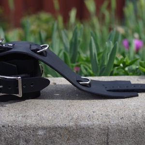 Puede incluir: Esposas de cuero negro con hebillas y anillas en D plateadas. Las esposas son ajustables y tienen un diseño sencillo.