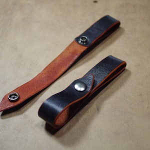 May include: Two leather straps with metal snaps. One strap is brown with a black edge, the other is black with a brown edge.