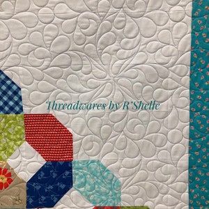 May include: A quilt with a white background and a swirling pattern. The quilt is made up of colorful squares with different patterns. The text "Threadwares by R'Shelle" is visible in the center of the quilt.