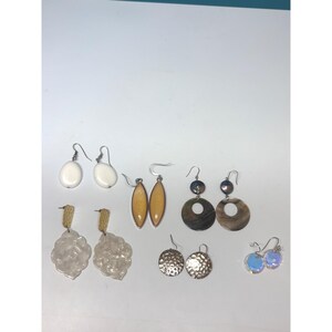 May include: A collection of six pairs of earrings featuring various designs: white teardrop dangles, yellow marquise shapes, dark circular discs, textured gold-tone studs, translucent floral-shaped dangles, and small iridescent circular dangles.
