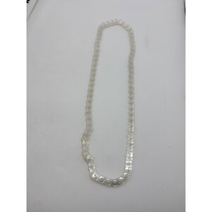 May include: A clear, transparent necklace composed of numerous circular, disc-shaped beads. The beads are strung together to form a long, elegant chain. The necklace is displayed against a plain white background.