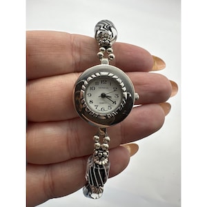 May include: A silver-toned Geneva quartz watch with a round face and a beaded bracelet. The watch face has black numerals and hands on a white background. The bracelet features decorative glass beads with black and white patterns.