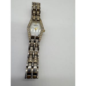 May include: A silver-toned Elgin watch with a geometric face and a band adorned with rhinestones. The watch face is a light color with gold-toned hands and the brand name "Elgin". The watch band is made of silver-toned metal.