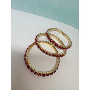 May include: Three circular bracelets featuring a gold-toned metal setting and a continuous row of round, faceted red stones. The bracelets are designed with a flexible, stretchable band construction, allowing them to expand for easy wear.