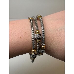 May include: A multi-strand wrap bracelet featuring silver-toned mesh chains accented with polished gold-toned spherical beads and ornate, engraved silver-toned cylindrical spacers. The design creates a layered appearance with metallic textures.