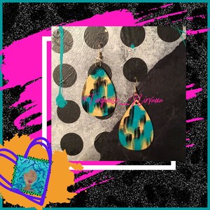 Puede incluir: Un par de pendientes en forma de lágrima con un diseño abstracto en negro, amarillo y turquesa. Los pendientes están sobre un fondo blanco con lunares negros.