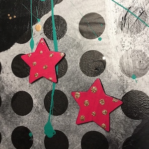 Puede incluir: Dos estrellas rosas con puntos de purpurina dorada sobre un fondo de lunares blanco y negro. El fondo también tiene salpicaduras de pintura turquesa.