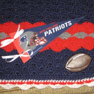 May include: A blue, red, and white crocheted blanket with a football and a pennant that says "New England Patriots".
