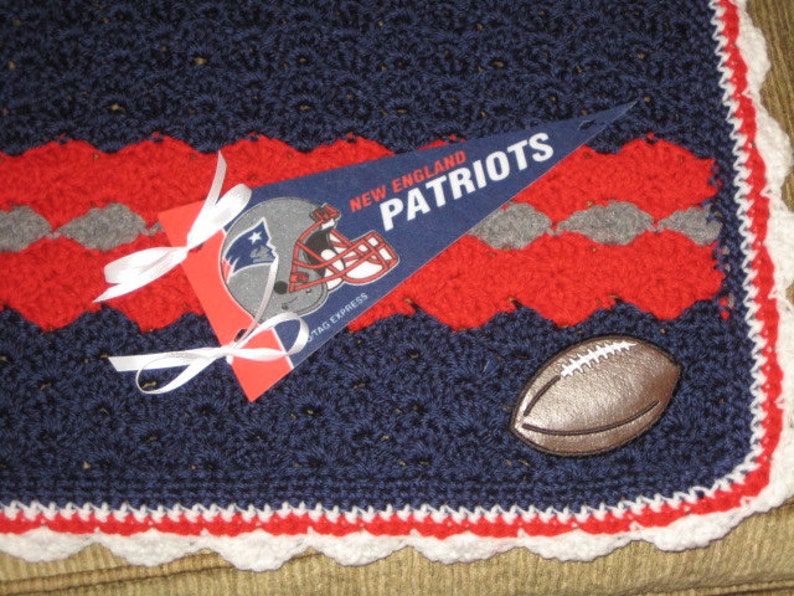 May include: A blue, red, and white crocheted blanket with a football and a pennant that says "New England Patriots".