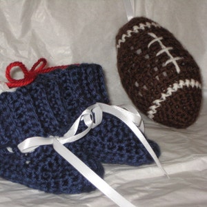 May include: A pair of blue crocheted baby booties with white ribbon ties, next to a brown crocheted football with white stitching.