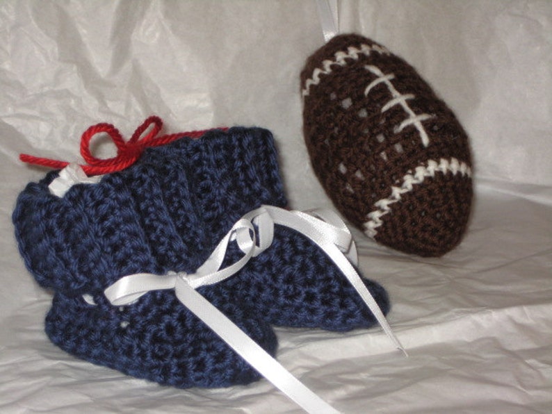 May include: A pair of blue crocheted baby booties with white ribbon ties, next to a brown crocheted football with white stitching.